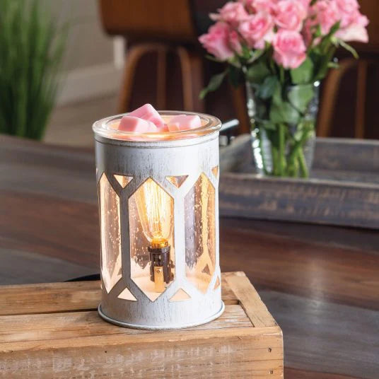 Decorative lantern with a lit candle on a wooden surface, with flowers in the background.