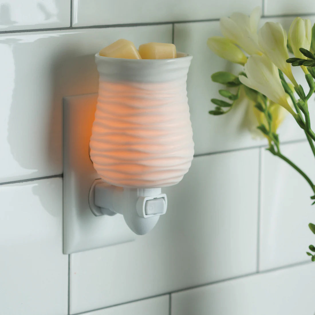 Wall-mounted night light emitting a warm glow on a tiled wall with flowers in the background.