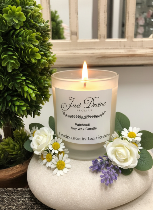 Candle labeled 'Just Divine' with flowers and greenery on a stone surface